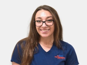Veterinary Assistant standing in front of a wall wearing blue scrubs that say PetSmart Veterinary Services